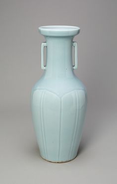 a light blue vase sitting on top of a white table next to a gray wall