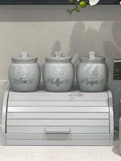 three gray jars sitting on top of a counter next to a white sink and towel dispenser