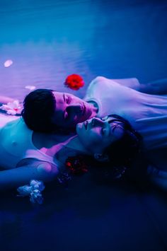 a woman laying on the ground next to a man in a white body suit and red rose