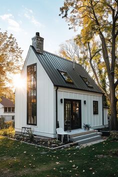 a small white house with a black metal roof and door on the front porch, surrounded by trees