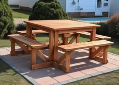 a wooden picnic table with two benches in front of a swimming pool and some bushes