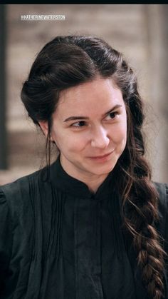 a woman with long hair wearing a black dress and smiling at the camera while standing in front of a building