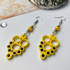 two pairs of yellow and black earrings sitting on top of a white table next to silverware