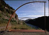 an arch made out of metal sitting on the side of a hill next to a river