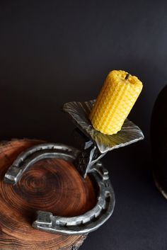 a yellow candle sitting on top of a piece of metal next to a wooden bowl