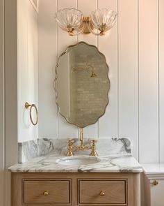 a bathroom vanity with marble counter top and gold faucet, two lights above it