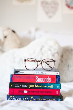 a stack of books sitting on top of a bed next to a pair of glasses