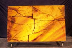 an abstract painting is displayed on a metal stand in front of a black backdrop with yellow and orange colors