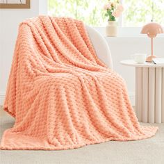 an orange blanket sitting on top of a chair next to a white table and window