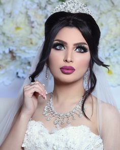 a woman wearing a wedding dress and tiara posing for a photo with flowers in the background