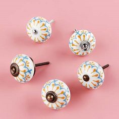 four ceramic door knobs and two handles on a pink surface with an orange, blue, yellow and white flower design