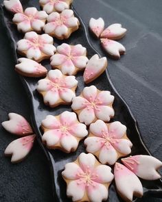 decorated cookies in the shape of flowers on a black platter with pink and white icing