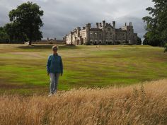 a woman standing in the middle of a field next to a large building on a cloudy day