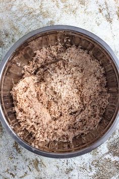 a metal bowl filled with brown stuff on top of a white countertop next to a wooden spoon