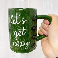 a hand holding a green coffee mug that says let's get cozy