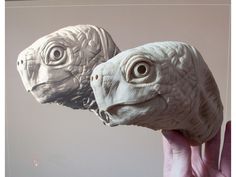 two sculptures of fish in the shape of heads, one being held up by a person's hand