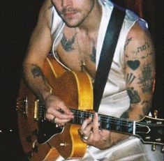 a man with tattoos playing an acoustic guitar