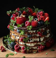 a cake with berries, strawberries and other toppings on a wooden table in front of a black background