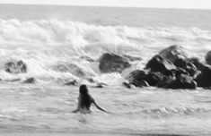 a woman wading in the ocean next to rocks