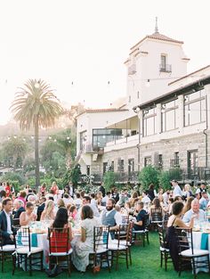 a large group of people sitting at tables in front of a building with palm trees