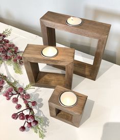 three wooden candle holders sitting on top of a white table next to flowers and candles