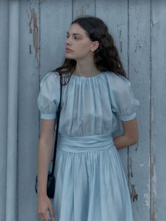 a woman in a blue dress leaning against a wall with her hand on her hip