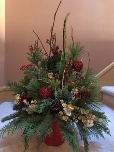 a red vase filled with lots of greenery and pine cones on top of a carpeted floor