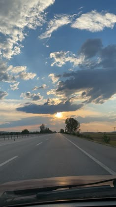 the sun is setting on an empty road with clouds in the sky and trees to the side