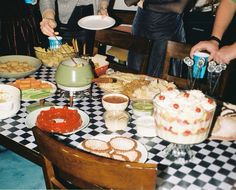 several people are standing around a table with food on it and plates in front of them