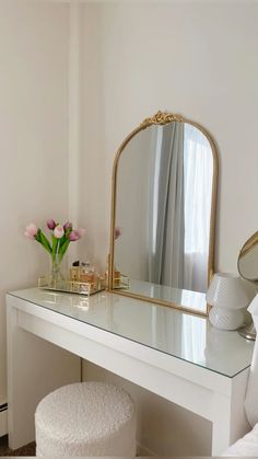 a white vanity with a mirror, stool and flowers on it in a bedroom setting