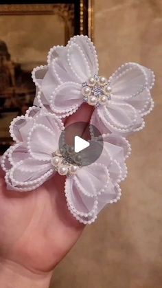 a hand holding two white flower clips with pearls on it's center and an oval button in the middle