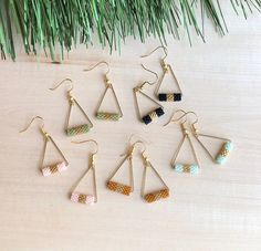 six pairs of earrings hanging from hooks on a wooden table next to pine needles and green grass