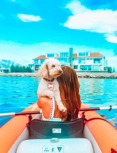 a woman and her dog are sitting in a boat on the water with houses in the background