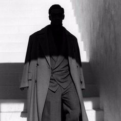 a black and white photo of a man in a suit standing next to some stairs