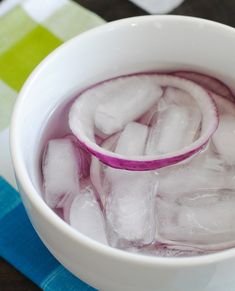 a white bowl filled with ice next to a blue and green table cloth on top of a wooden table