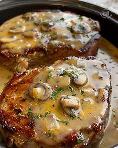 two pork chops covered in mushrooms and gravy on top of a skillet