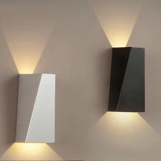 two modern wall lights mounted to the side of a white and black wall next to each other