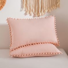 a pink pillow with pom - poms on it next to a wall hanging