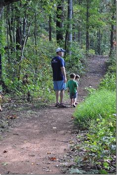 a man and child walking down a dirt path in the woods