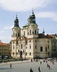 people are walking around in front of a large building with two towers and three spires