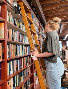 a woman standing on a ladder in front of a bookshelf filled with books