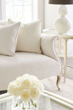 a living room with white furniture and flowers in a vase on the coffee table next to the couch