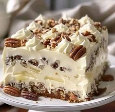 a piece of cake with white frosting and pecans on top is sitting on a plate