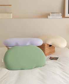 two pillows sitting on top of a white bed next to a wicker basket filled with books