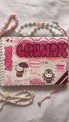 a hello kitty notebook is laying on a white sheet with beads and pearls around it