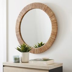 a round mirror hanging on the wall above a dresser with a potted plant next to it