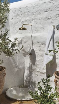 an outdoor shower with olive trees and towels hanging from it's hooks in front of a white stucco wall