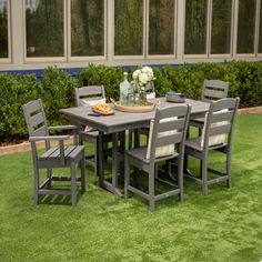 a table and chairs sitting on top of a green grass covered field next to windows