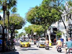 people are riding bikes and cars on the street in front of buildings with palm trees