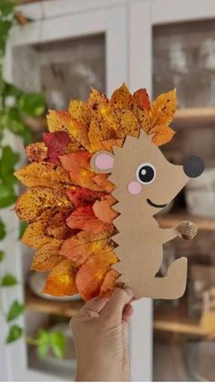 a hand holding up a paper hedge with autumn leaves on it's head and eyes